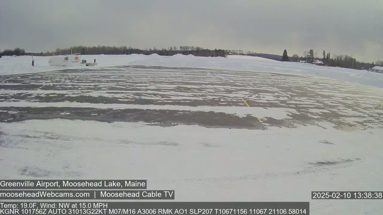A snow-covered airport tarmac with a few buildings in the background under an overcast sky.