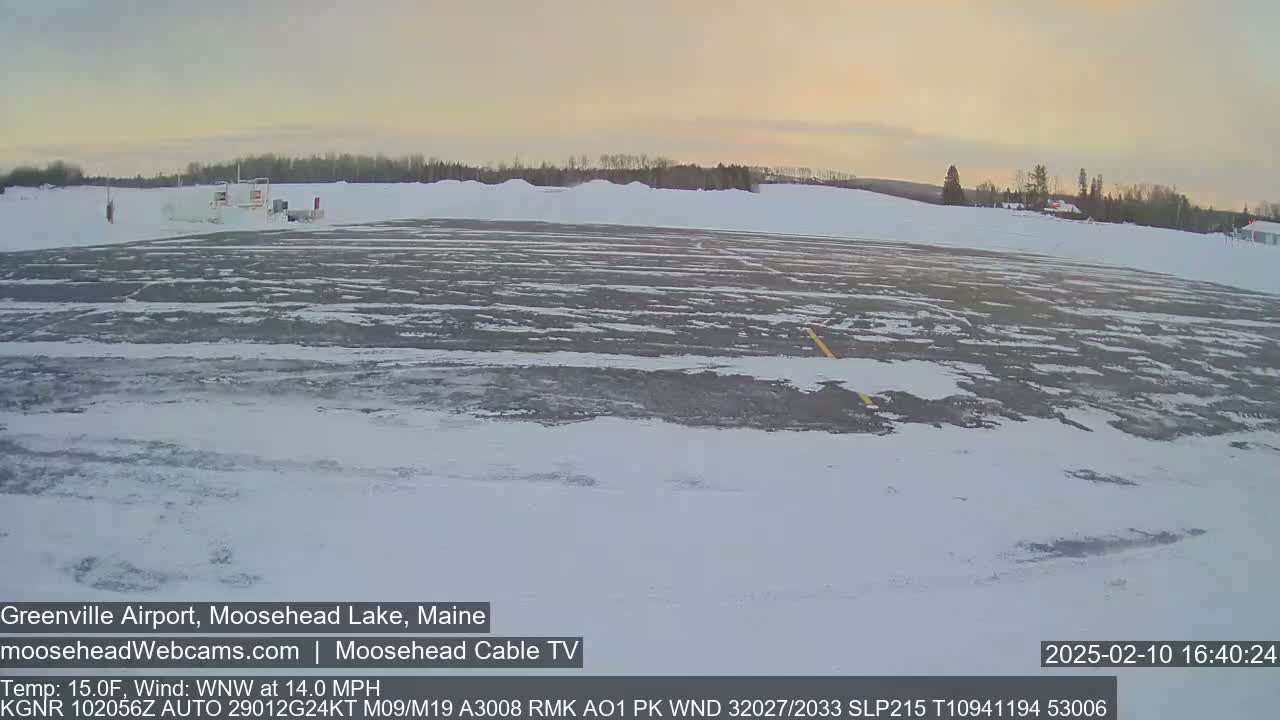 A snow-covered airport tarmac with a building in the distance under a pale, twilight sky.