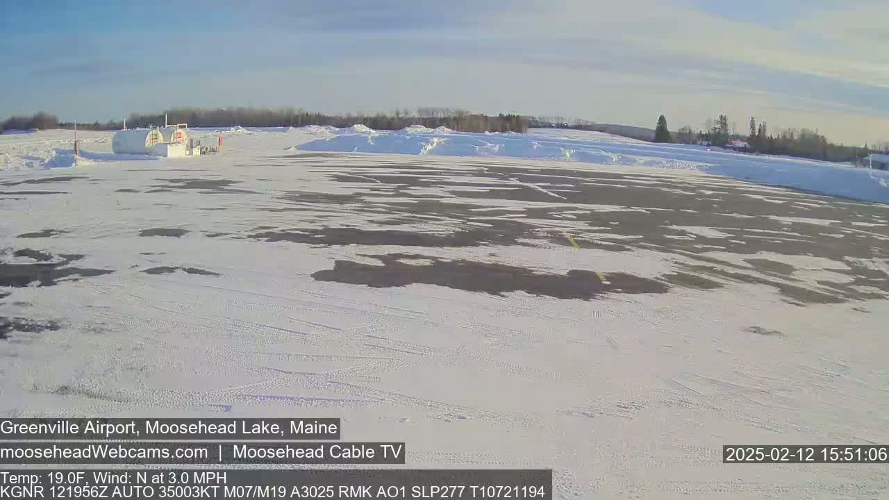 A snow-covered airfield with a small fuel depot is visible under a sunny sky.