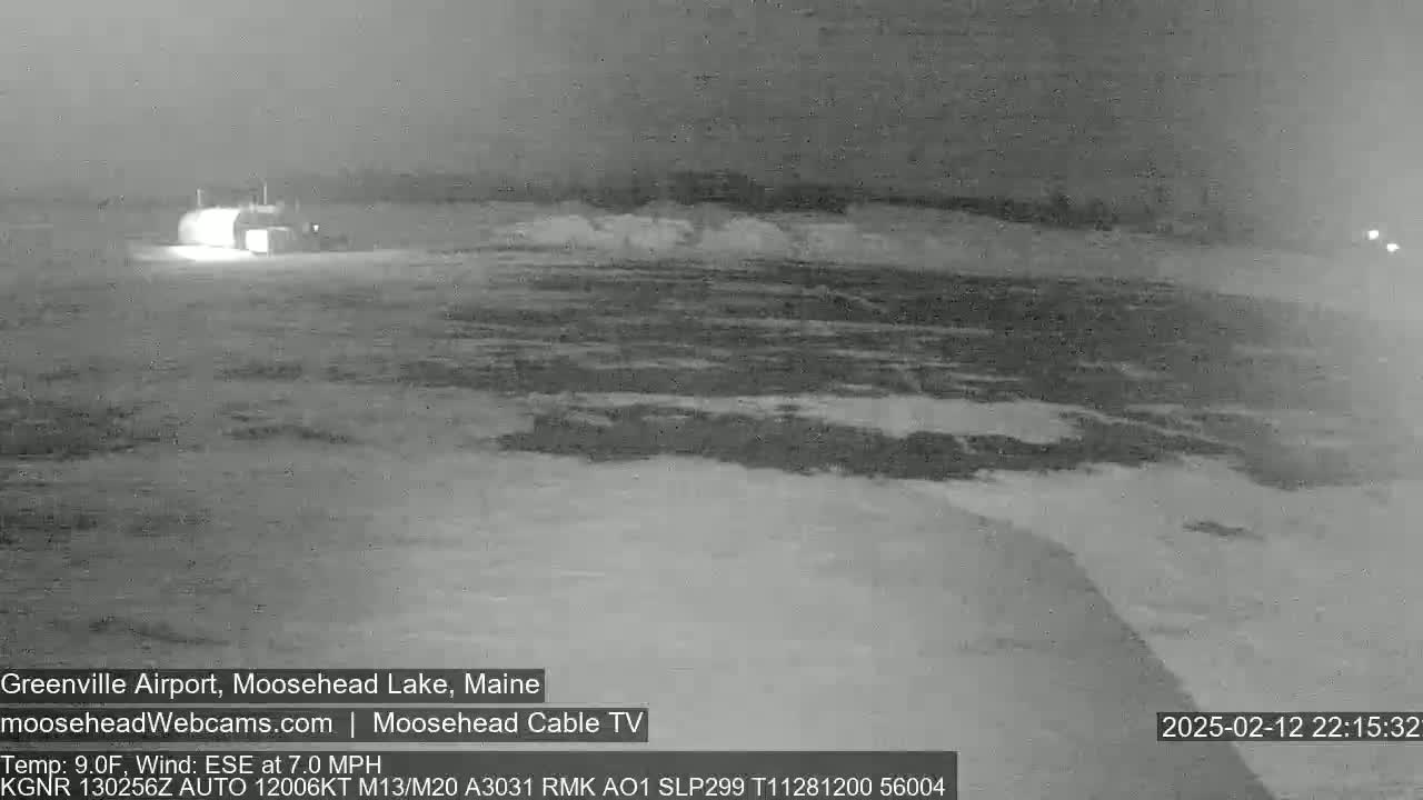 A nighttime, snow-covered airfield is visible under a dark sky, with a building faintly illuminated in the distance.