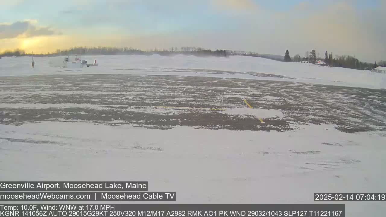A snow-covered airport runway is visible at sunrise, with a light wind blowing.