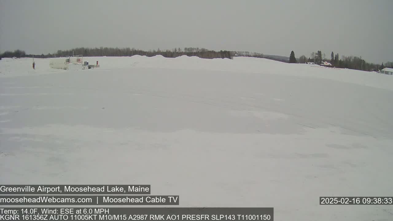 A snow-covered landscape stretches out under an overcast sky, with a few buildings visible in the distance.
