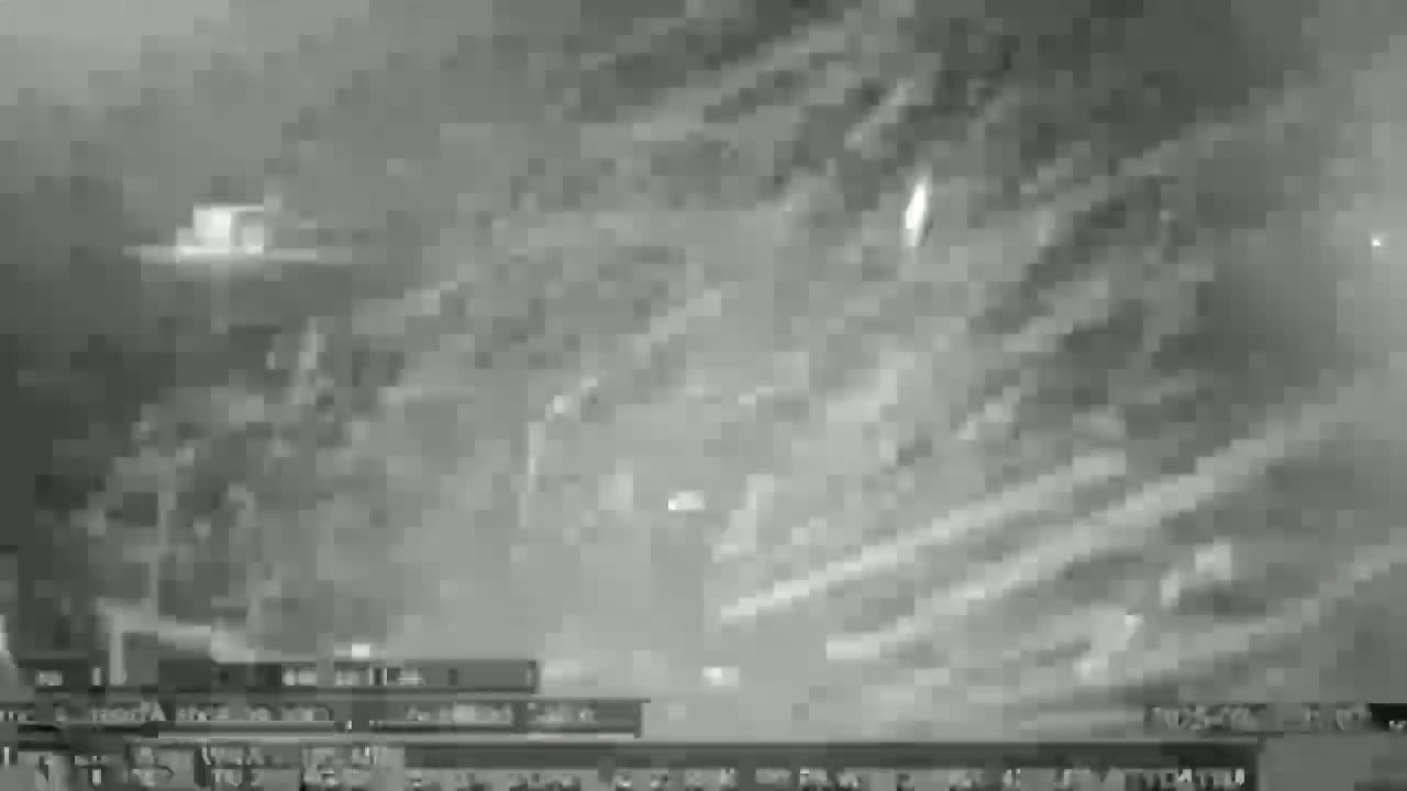 A blurry, grayscale image shows a nighttime scene with heavy cloud cover obscuring the view of buildings and structures below.