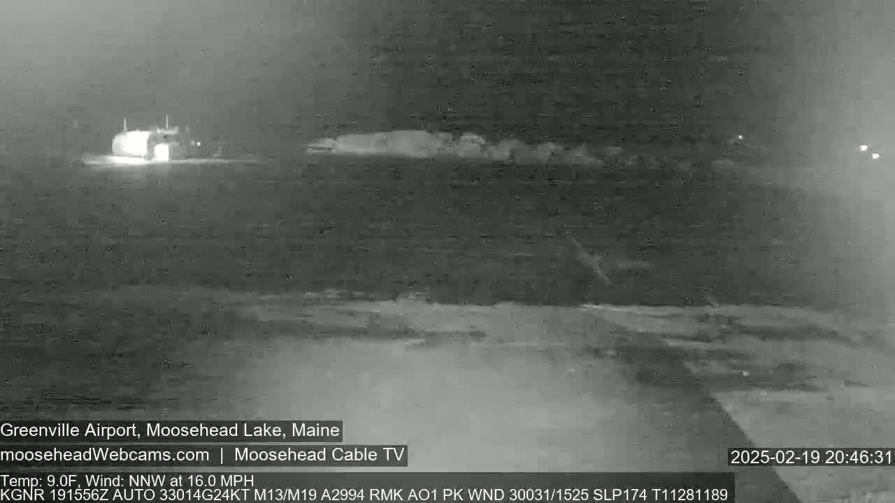 A nighttime, low-visibility view of a body of water with a building faintly visible in the distance, under a north-northwest wind of 16 mph and a temperature of 9 degrees Fahrenheit.