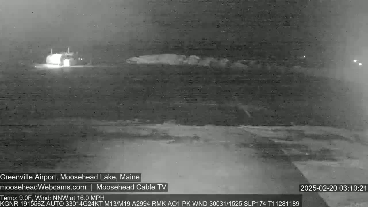 A nighttime, low-visibility view of a building, possibly an airport hangar, with a north-northwest wind at 16 mph and a temperature of 9°F.