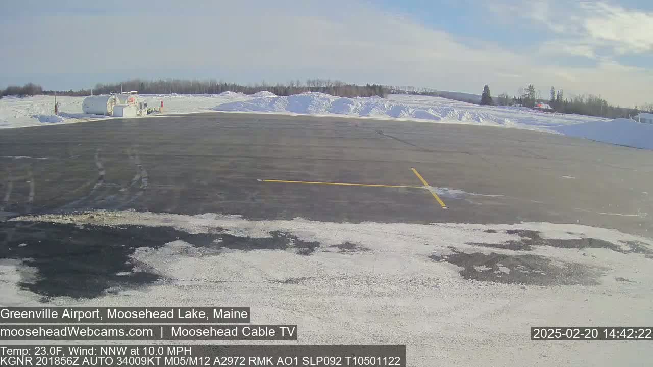A mostly clear, sunny day shows a snow-covered airfield with a fuel depot and distant trees.