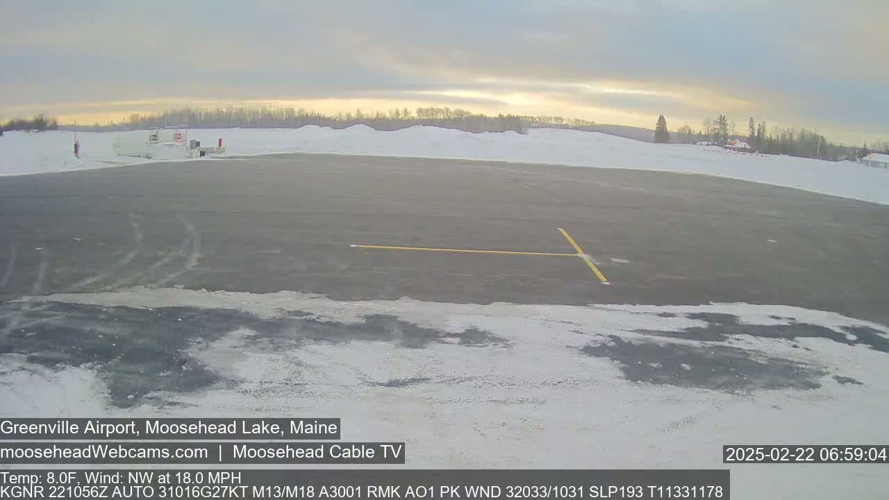 A mostly empty snow-covered airport tarmac with a building in the background under a partly cloudy sky.