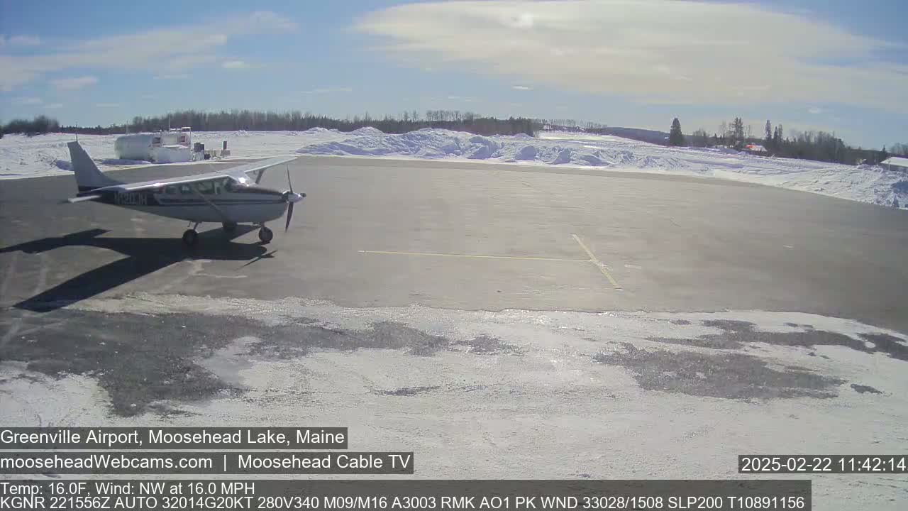 A small airplane sits on a snowy airport tarmac under a mostly sunny sky.