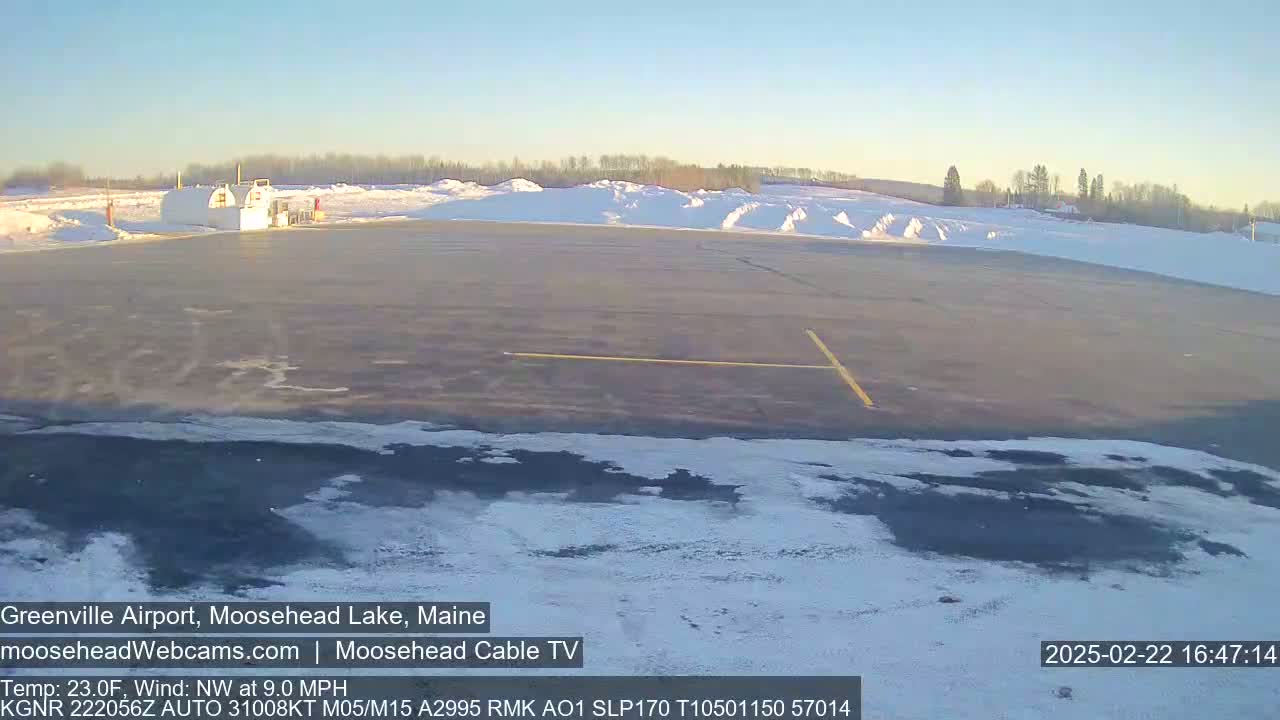 A mostly clear, cold, and slightly windy day at a snow-covered airport with a small building in the background.