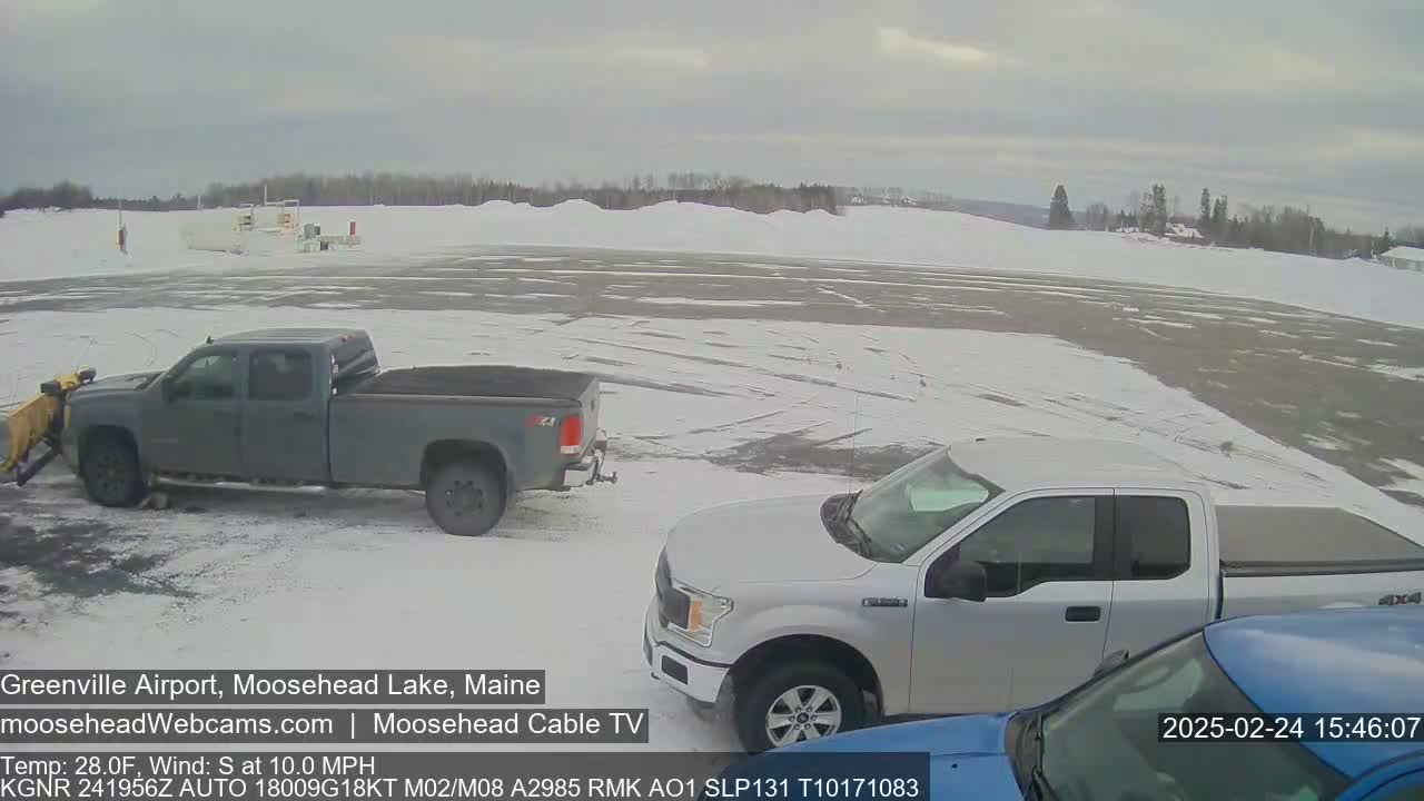 A snow-covered airport tarmac with a gray pickup truck and a silver pickup truck parked, under an overcast sky.