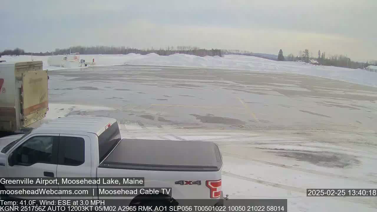 A mostly snow-covered airfield is viewed from a truck's perspective, under a cloudy sky.