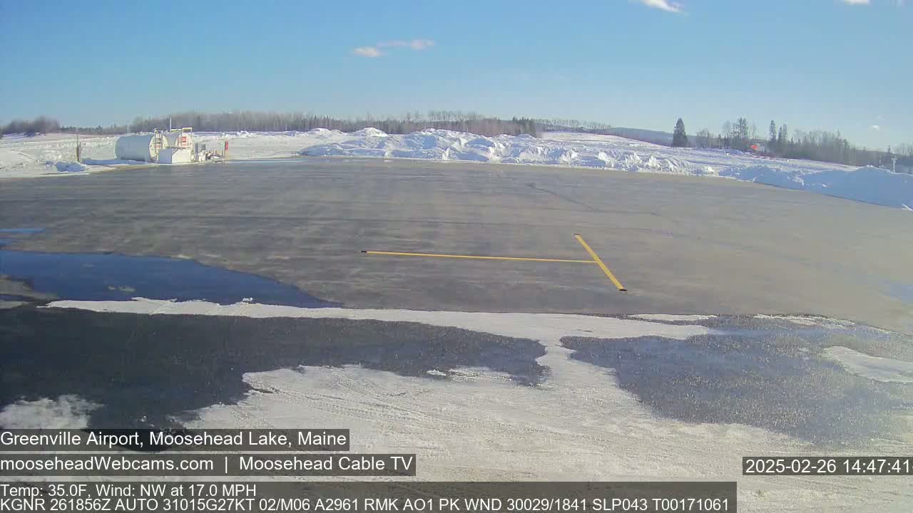 A mostly empty airport tarmac with snow and ice patches, under a clear blue sky.