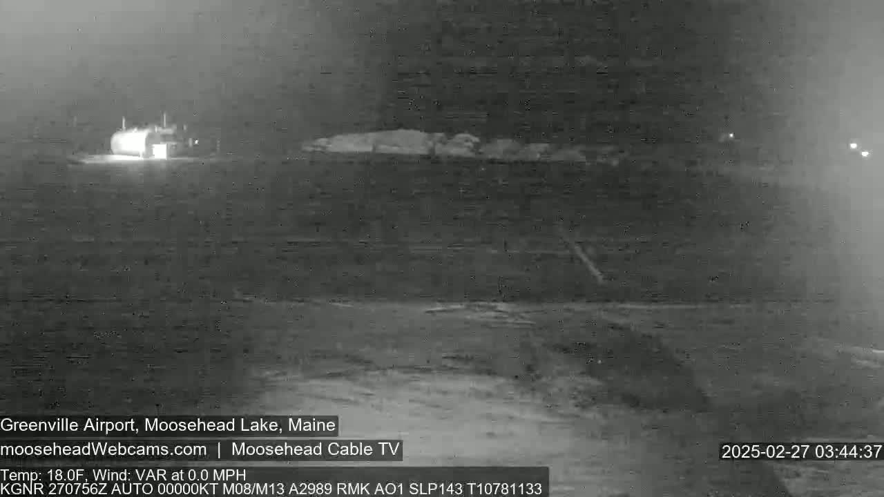A nighttime, low-visibility shot of a small building and a mostly empty, dark expanse of land, with a temperature of 18 degrees Fahrenheit.