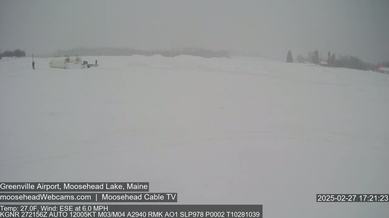 A snow-covered, flat landscape with a few vehicles visible in the distance under heavy snowfall.