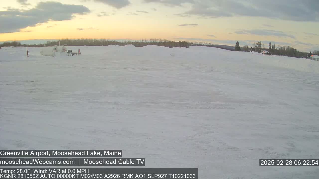 A snow-covered airfield is visible at sunrise, with a few vehicles parked near a treeline in the distance.