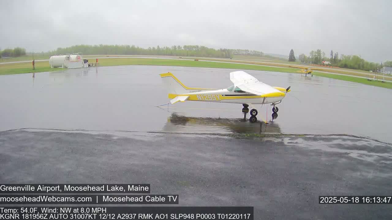 A wet airport tarmac with two small airplanes parked, under an overcast sky.