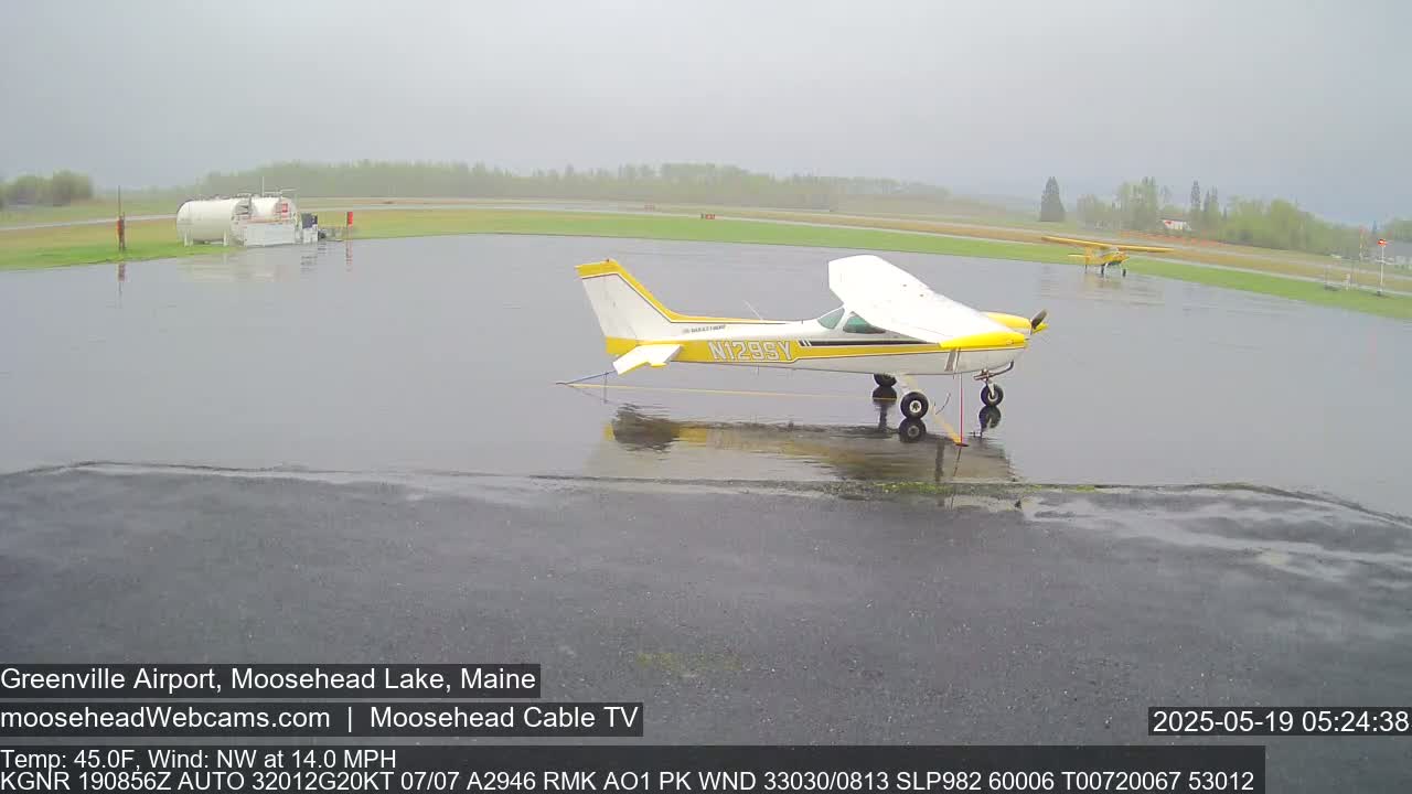 Two small airplanes sit on a rain-soaked tarmac at an airport.