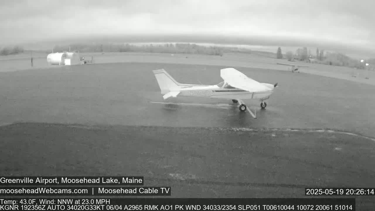 A small airplane is taxiing on a wet tarmac at an airport under an overcast sky.