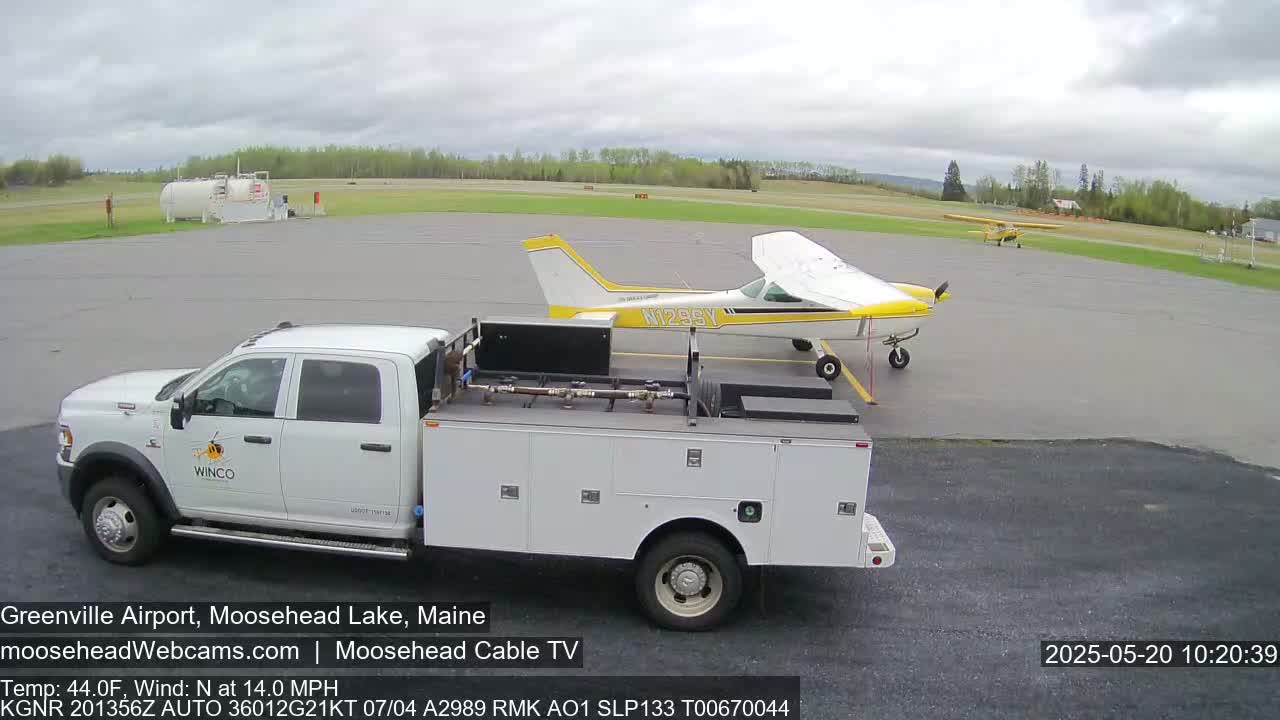 A white pickup truck is parked next to a yellow and white airplane on a tarmac under a partly cloudy sky.