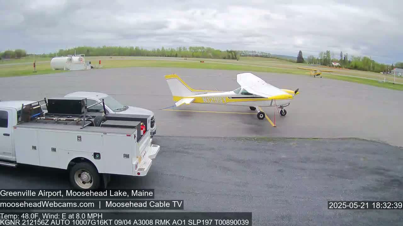 A small airplane and a pickup truck are parked on an airport tarmac under a partly cloudy sky.
