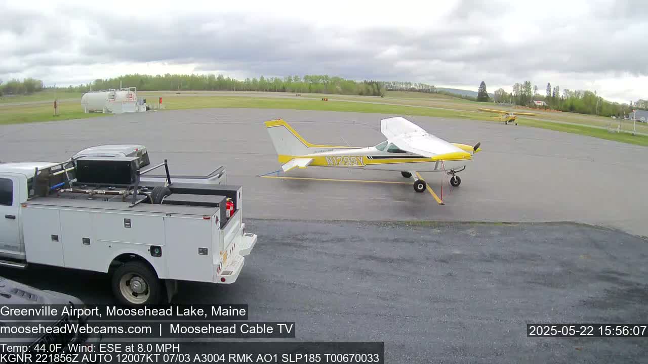 A small, yellow and white airplane is parked on a tarmac next to a pickup truck on an overcast day.
