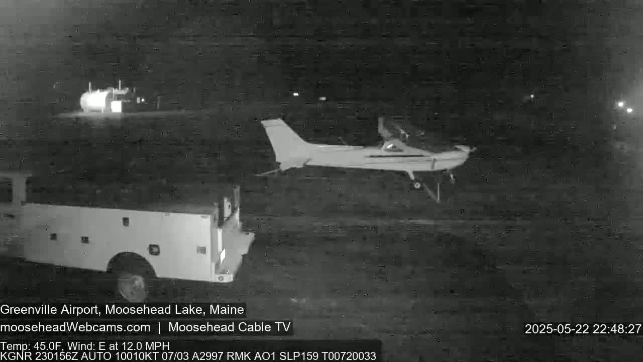 A small airplane is on the ground near a truck at night with an east wind at 12 mph and a temperature of 45 degrees Fahrenheit.