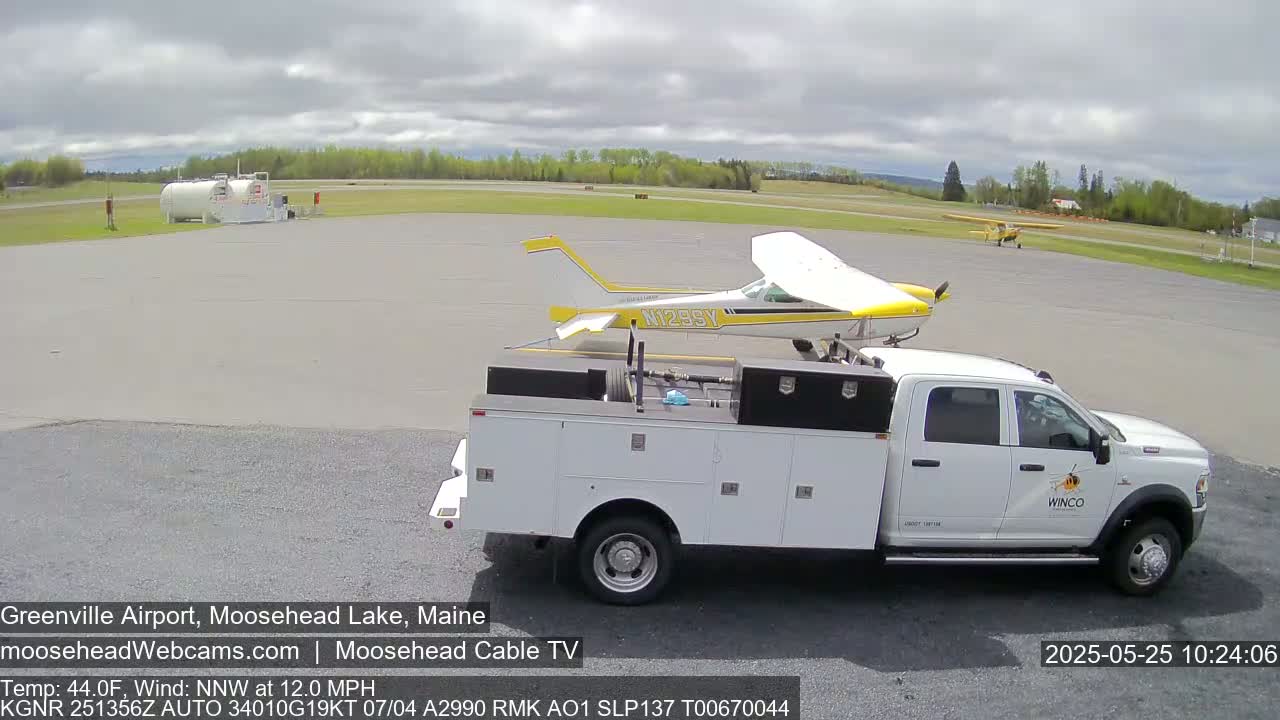 A small yellow and white airplane is parked next to a white service truck at an airport on an overcast day.