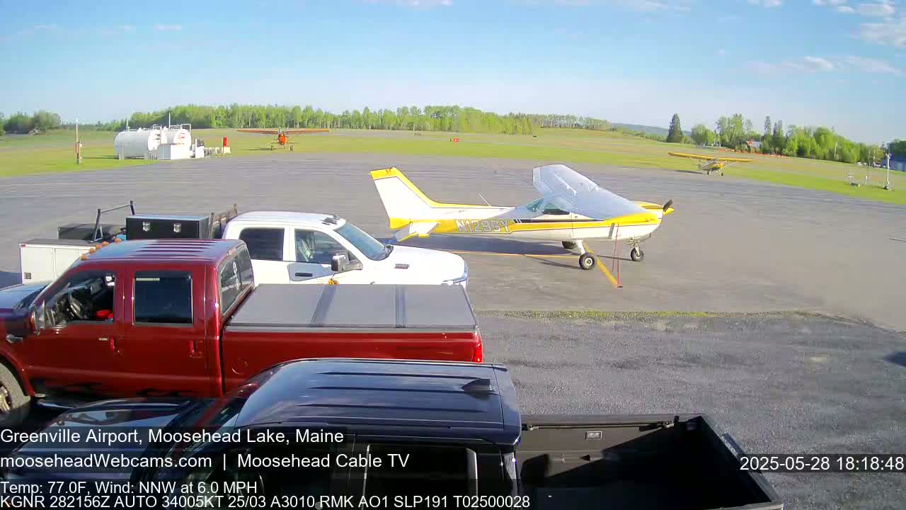 On a sunny day, several small airplanes are parked on an airfield next to several pickup trucks.