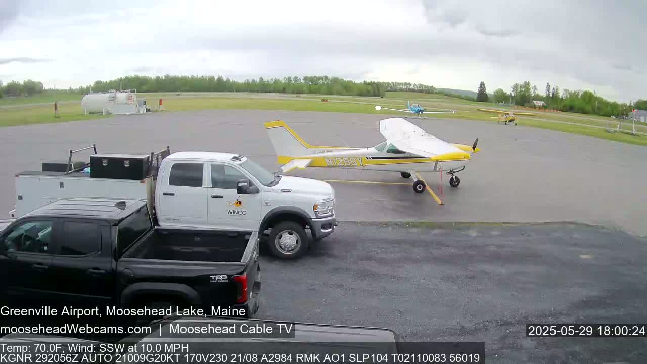 Two small airplanes are parked on an airport tarmac, with two pickup trucks nearby, under an overcast sky.