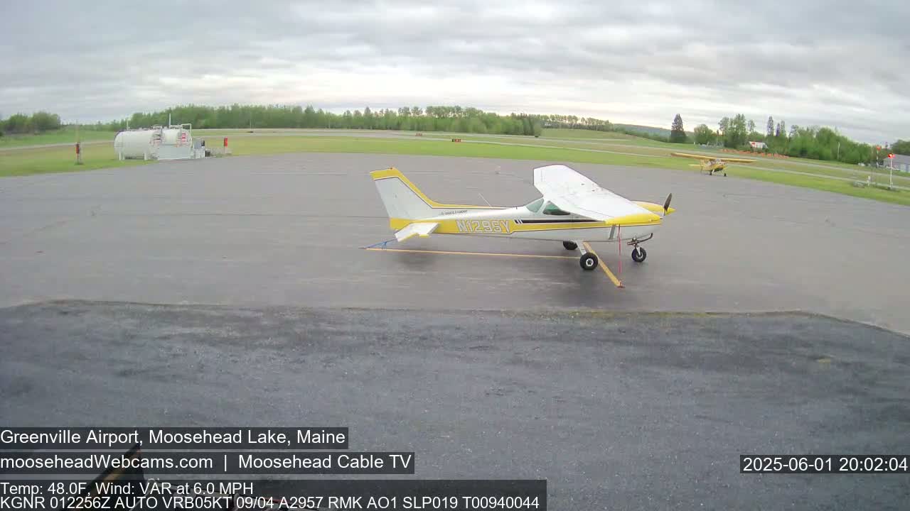 A yellow and white single-engine airplane is parked on a tarmac at an airport under an overcast sky.