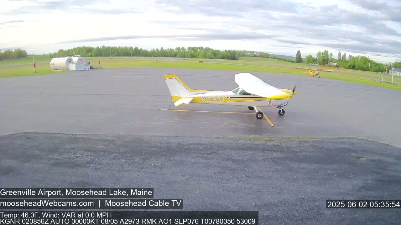 A yellow and white single-engine airplane is parked on a tarmac at an airport under a partly cloudy sky.