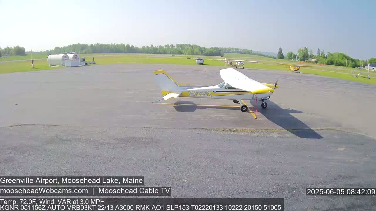 A small airport tarmac on a sunny day with several small airplanes parked, one prominently in the foreground.