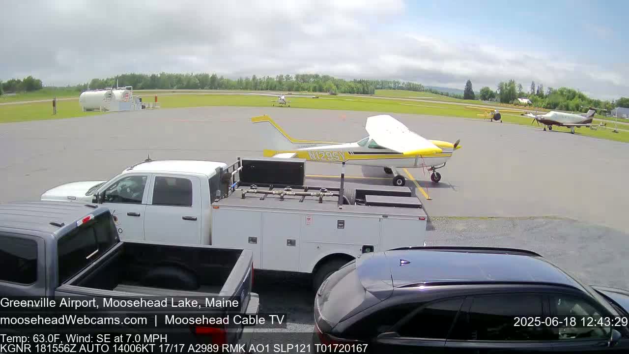 On a sunny day with a southeast wind, several small planes are parked on an airport tarmac next to service trucks and cars.