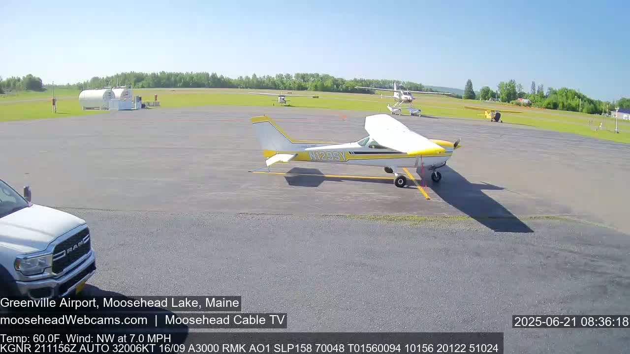 A small airport tarmac with several small airplanes parked, under sunny skies.