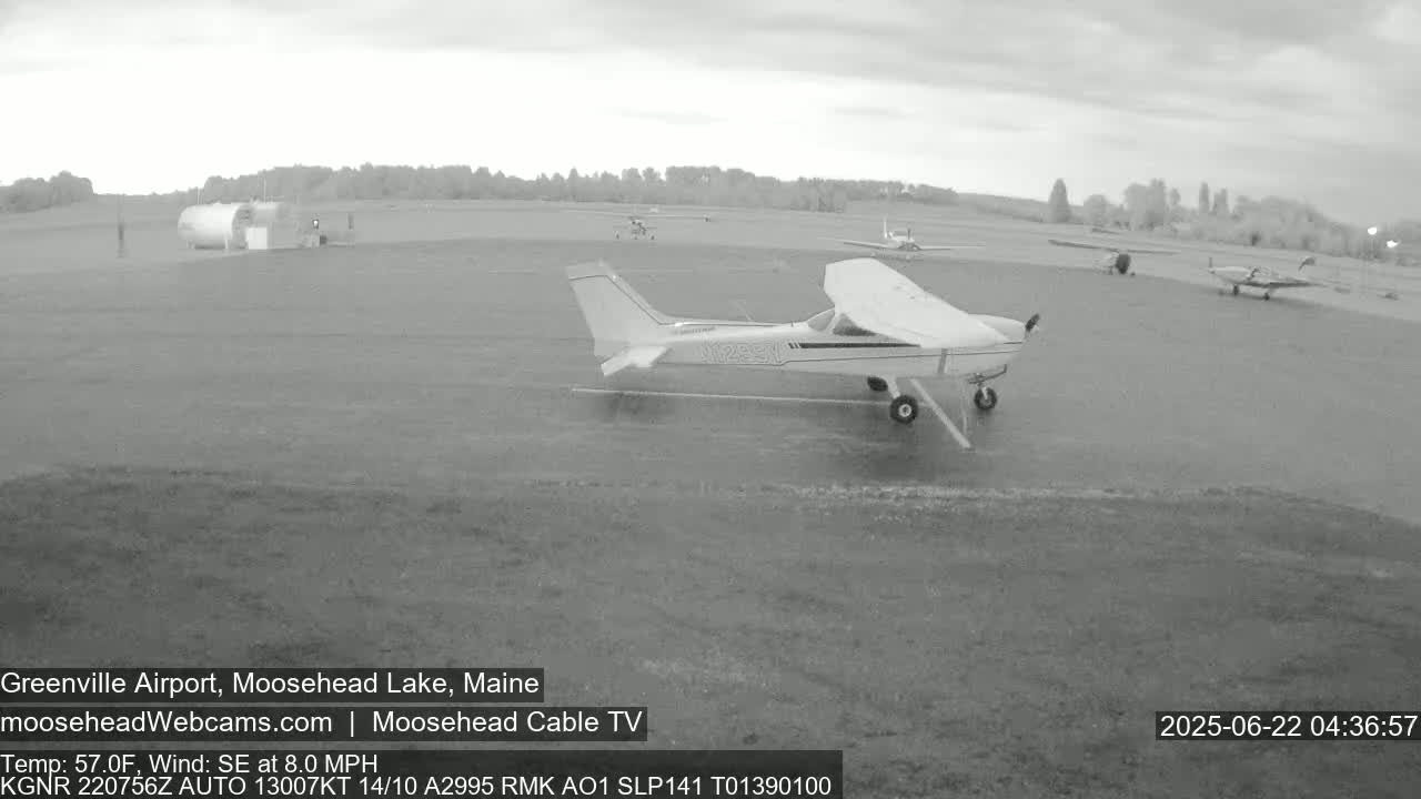 Several small airplanes are parked on a wet tarmac at an airfield under an overcast sky.