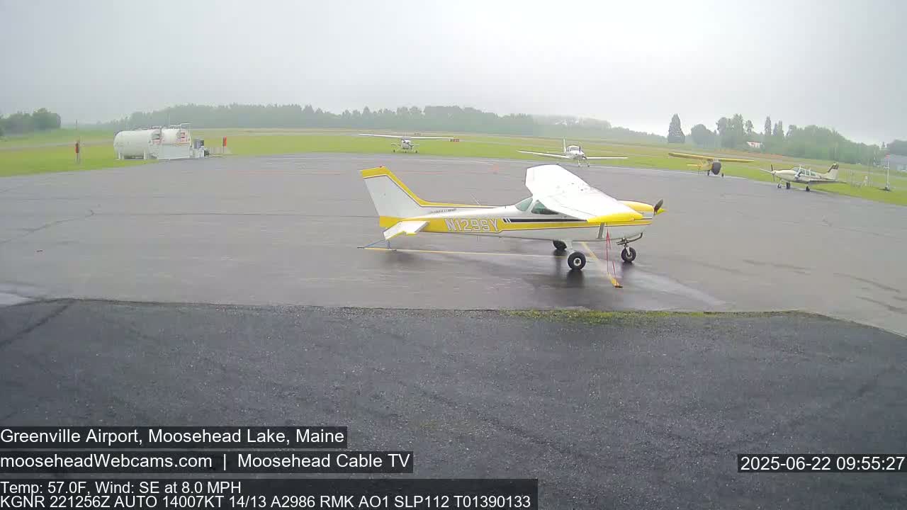 Several small airplanes are parked on a wet tarmac at an airport in rainy conditions.