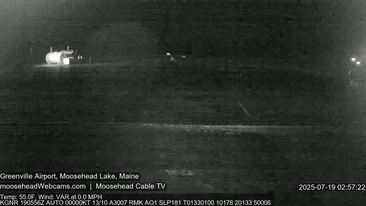 A nighttime, low-light image shows a building and a vehicle, with calm weather conditions.