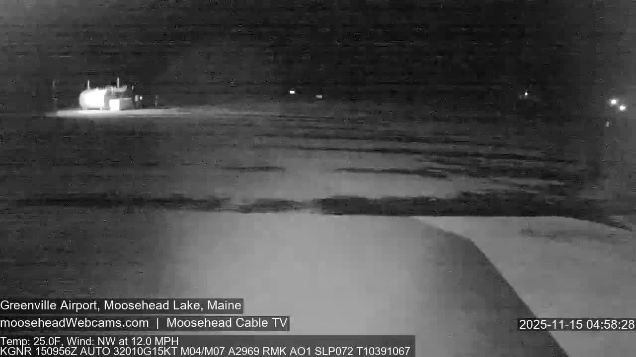 A dark, wide-angle outdoor nighttime scene depicts a brightly illuminated cylindrical structure with associated equipment in the mid-ground, surrounded by a few distant, fainter lights, all under a clear night sky over dark, textured ground.