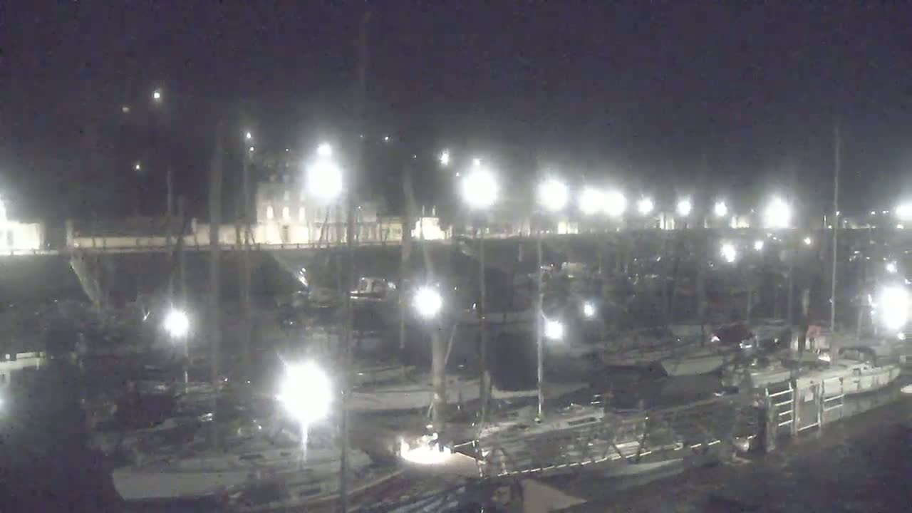 Many boats are docked at a marina at night under bright lights.