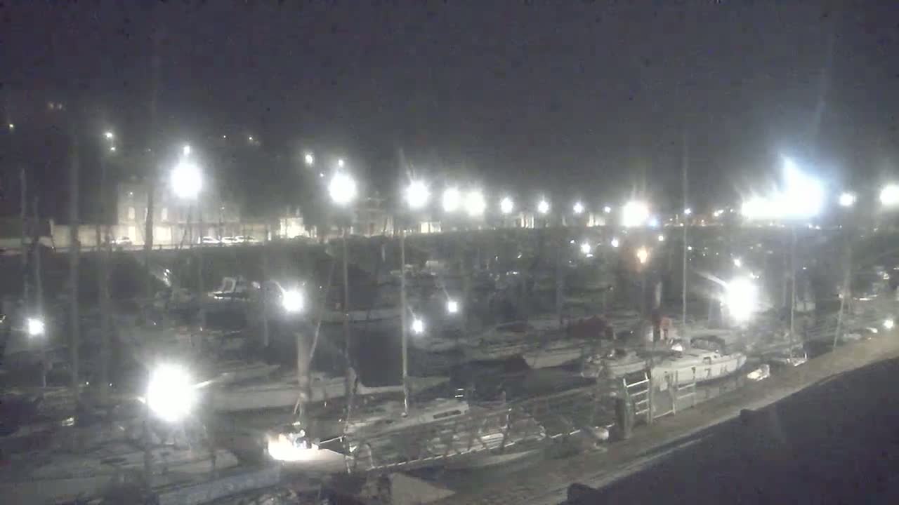 A nighttime view of a marina filled with numerous boats illuminated by bright lights.