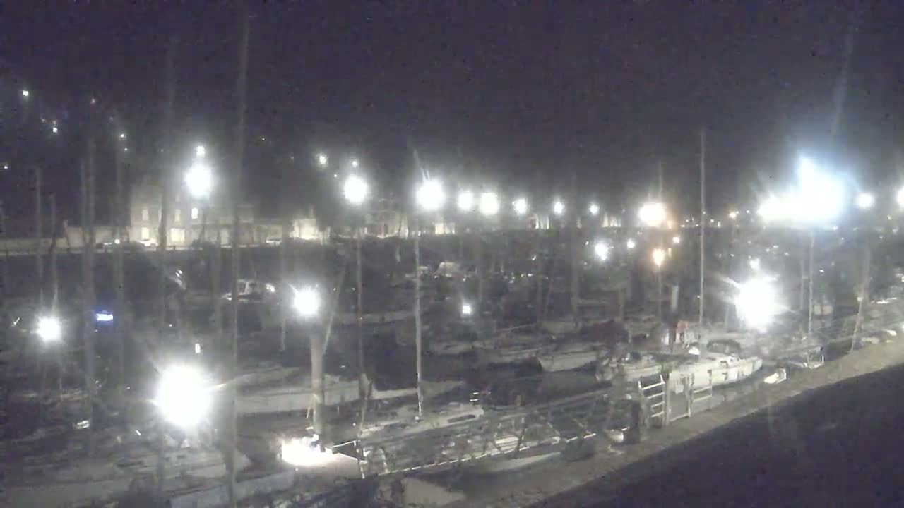 A nighttime view of a marina filled with sailboats illuminated by many bright lights.