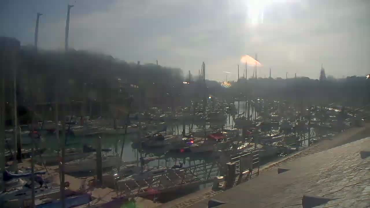 A hazy sun shines over a marina filled with many boats docked at various points.