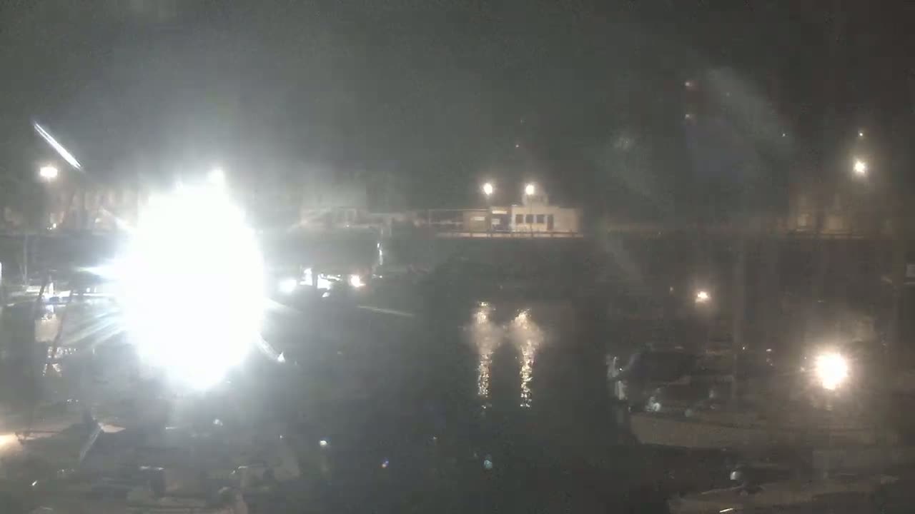 A brightly lit area near a body of water at night, shrouded in fog or mist.
