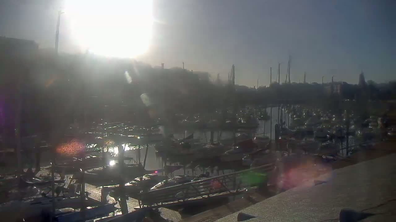 A hazy sunrise illuminates a marina filled with numerous boats moored in calm water.