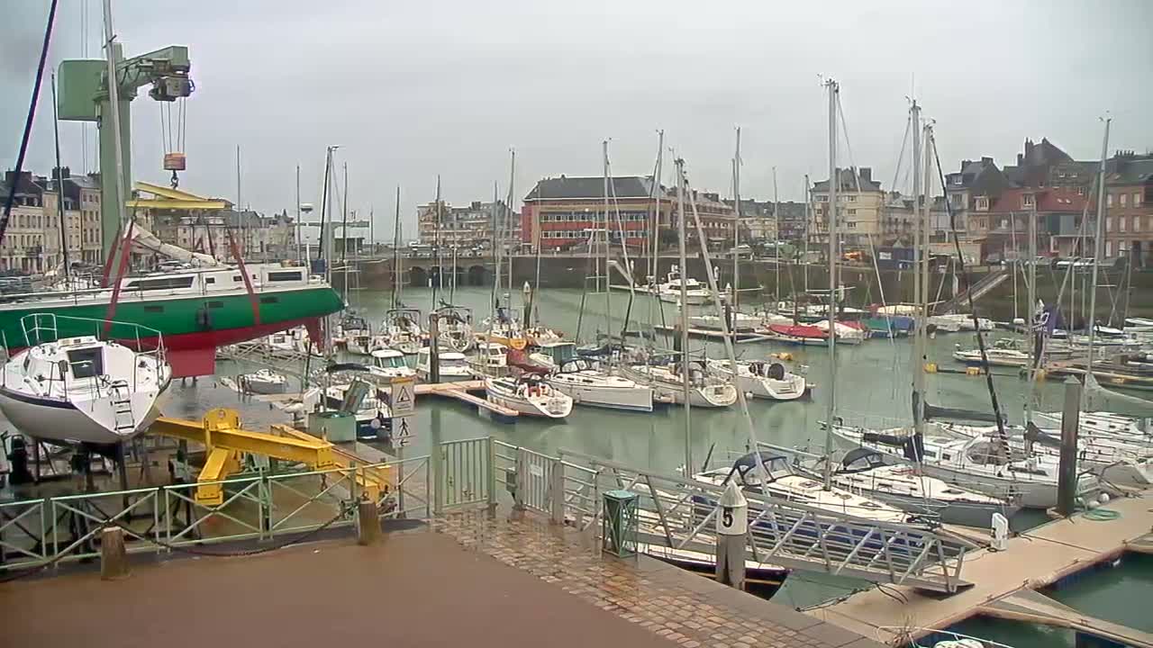 A marina filled with numerous sailboats on a cloudy day, with one sailboat being lifted by a crane.