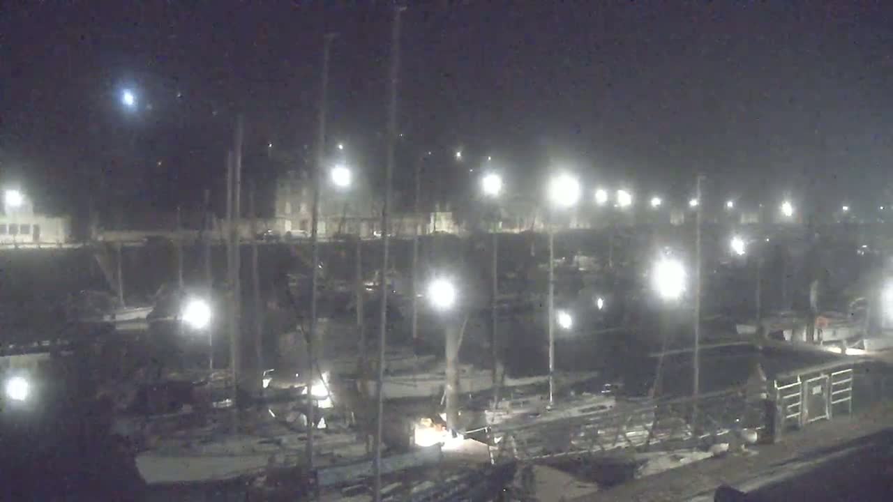 A nighttime view of a marina filled with sailboats under illuminated artificial light.
