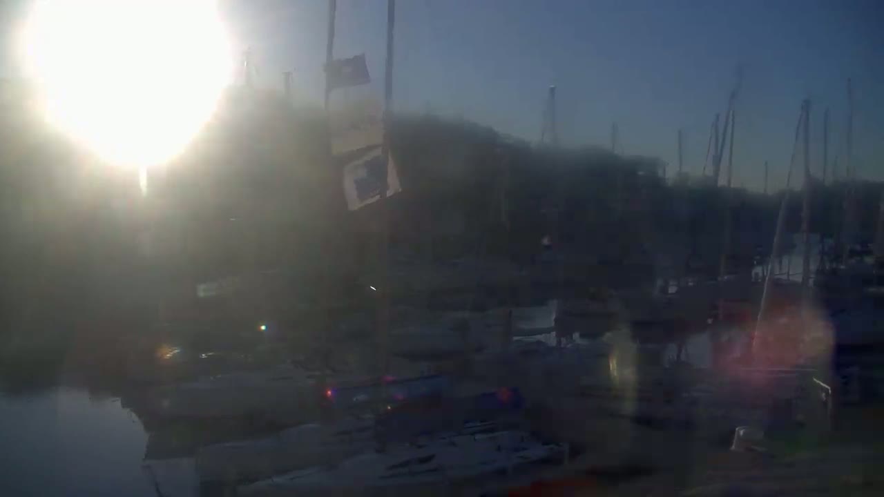 A hazy sunrise illuminates a marina filled with numerous boats and masts.