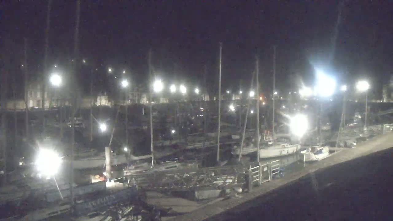 A nighttime view of a marina filled with boats under bright artificial lights.