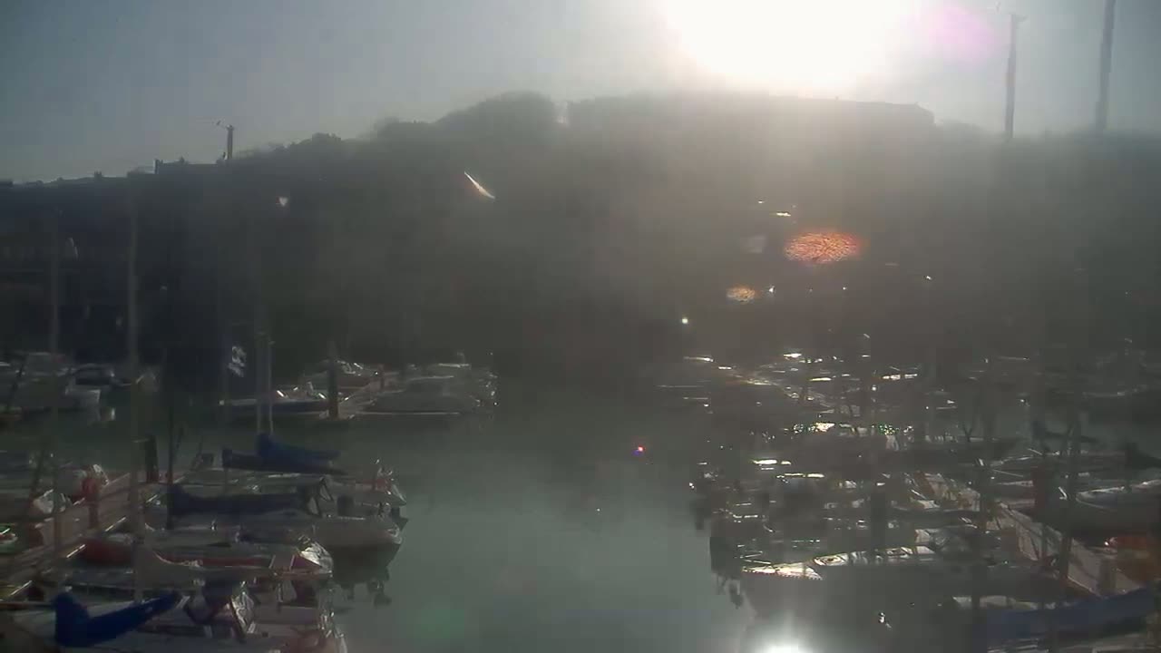 A hazy sunrise illuminates a marina filled with numerous boats docked along piers.