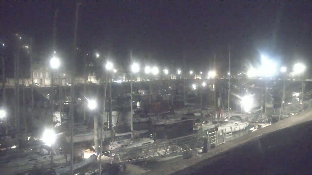 A nighttime view of a marina filled with docked sailboats illuminated by bright lights.